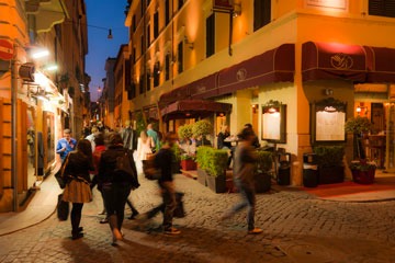 people walking at nightfall across an intersection in Rome, Italy