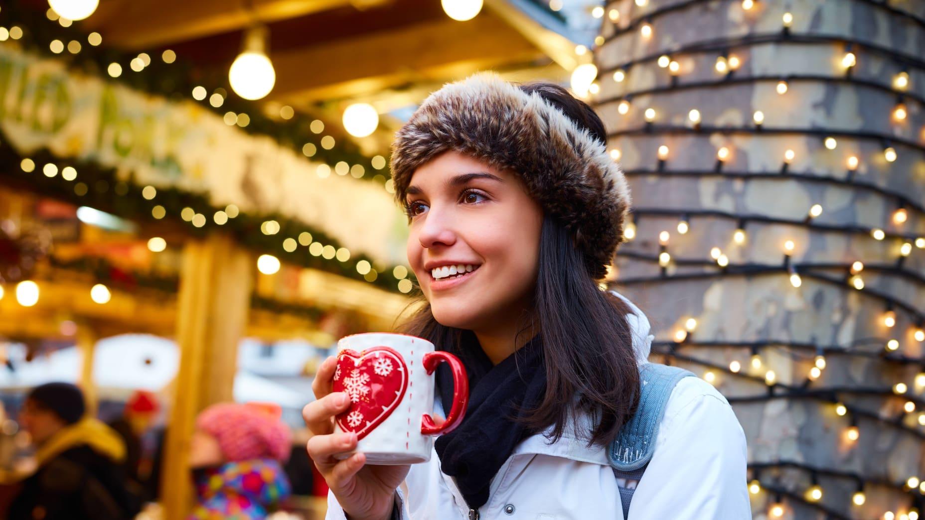 A woman stands with a cup of mulled wine at a festively decorated Christmas market.