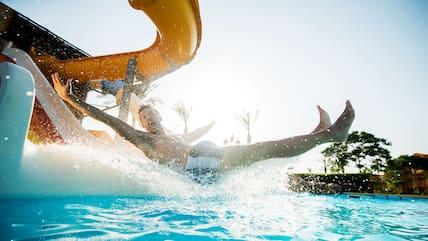A man splashes into a pool from a water slide with a lot of spray.