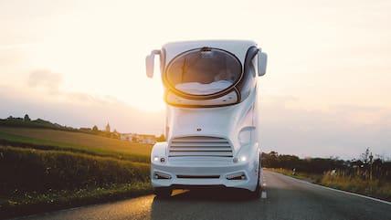 A gigantic white motorhome on a road at sunset.
