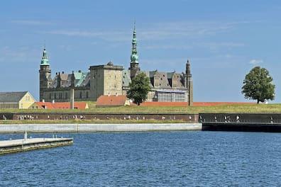 View over a blue bay to Kronborg Castle in Helsingør, with a tower rising in the middle