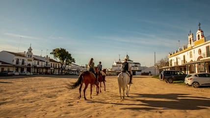 Two people riding horses through a street in the village of El Rocío in Andalusia