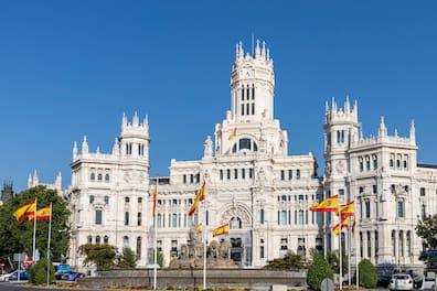 The Palacio de Cibeles from outside during the day with a fountain and Spanish flags.
