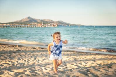 A toddler runs joyfully on a beach on the Balearic Island of Mallorca.