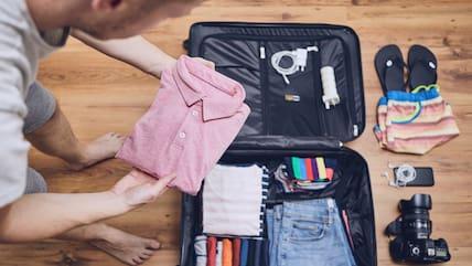 A man packing a carry-on suitcase.