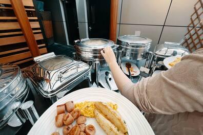 A lady choosing food from a warming tray at the hotel buffet to put it on her plate.