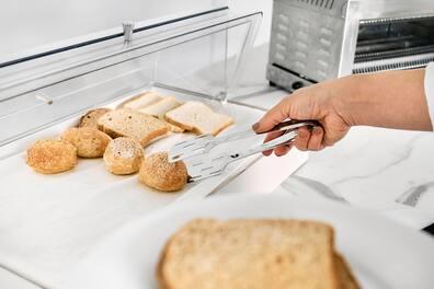A woman's hand taking a roll with a serving tong from a hotel restaurant.