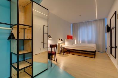 Double room in the MEININGER Hotel Leipzig with modern light design, desk, and mirrored wardrobe with shelves
