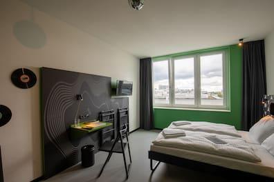 Double room in the MEININGER Hotel Dresden with bed, desk, and green-framed window