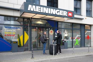Building of the MEININGER Hotel Berlin Central Station with large letters MEININGER, below two men talking and inscription 'Come in, leave as a friend' on the window