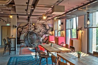 View into a lounge at the MEININGER Hotel Berlin Tiergarten with wooden tables and hanging chairs