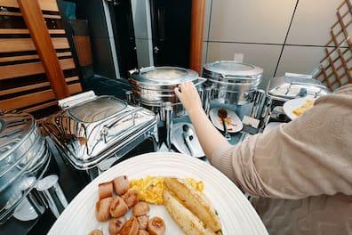 A lady at the hotel buffet selecting food from a warmer to put on her plate.