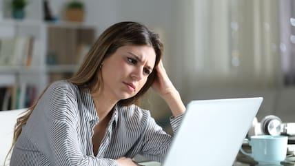 A woman sits with a questioning face in front of a laptop.
