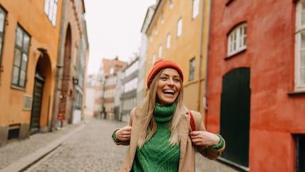 A smiling woman walks through a street with colorful houses.