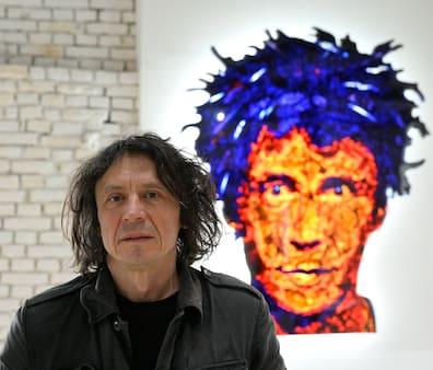 A man stands in a room with an abstract self-portrait in the background.