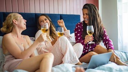 Friends having fun while drinking wine and chatting in the bedroom