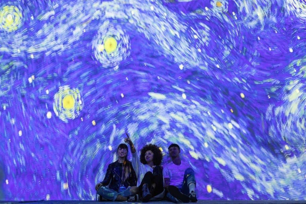 three people admiring the starry night projection at the Van Gogh exhibition