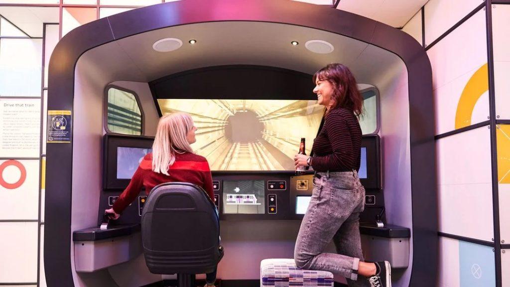 two women in front of tube simulator, one holding a beer